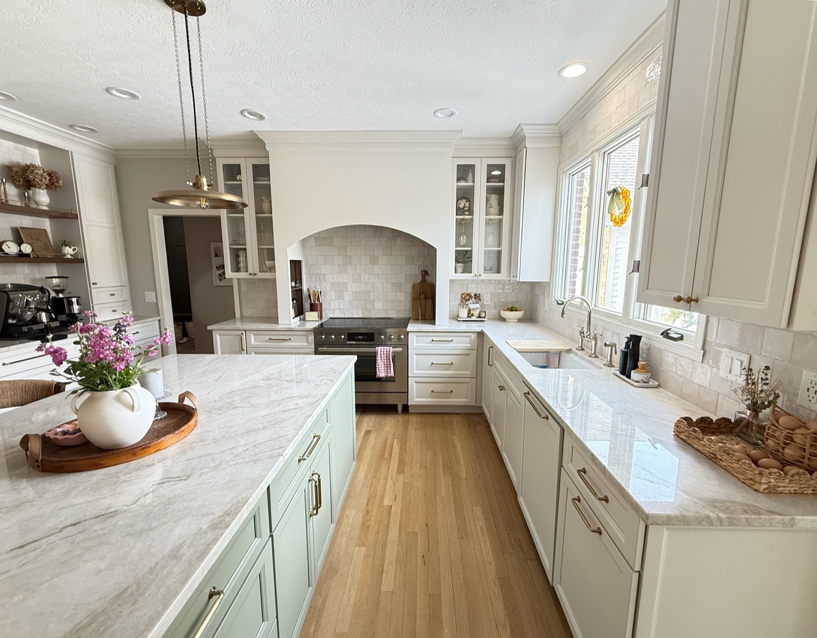 Full kitchen remodel with a sage-green island, quartzite countertops, white perimeter cabinetry, and brass pendant lighting